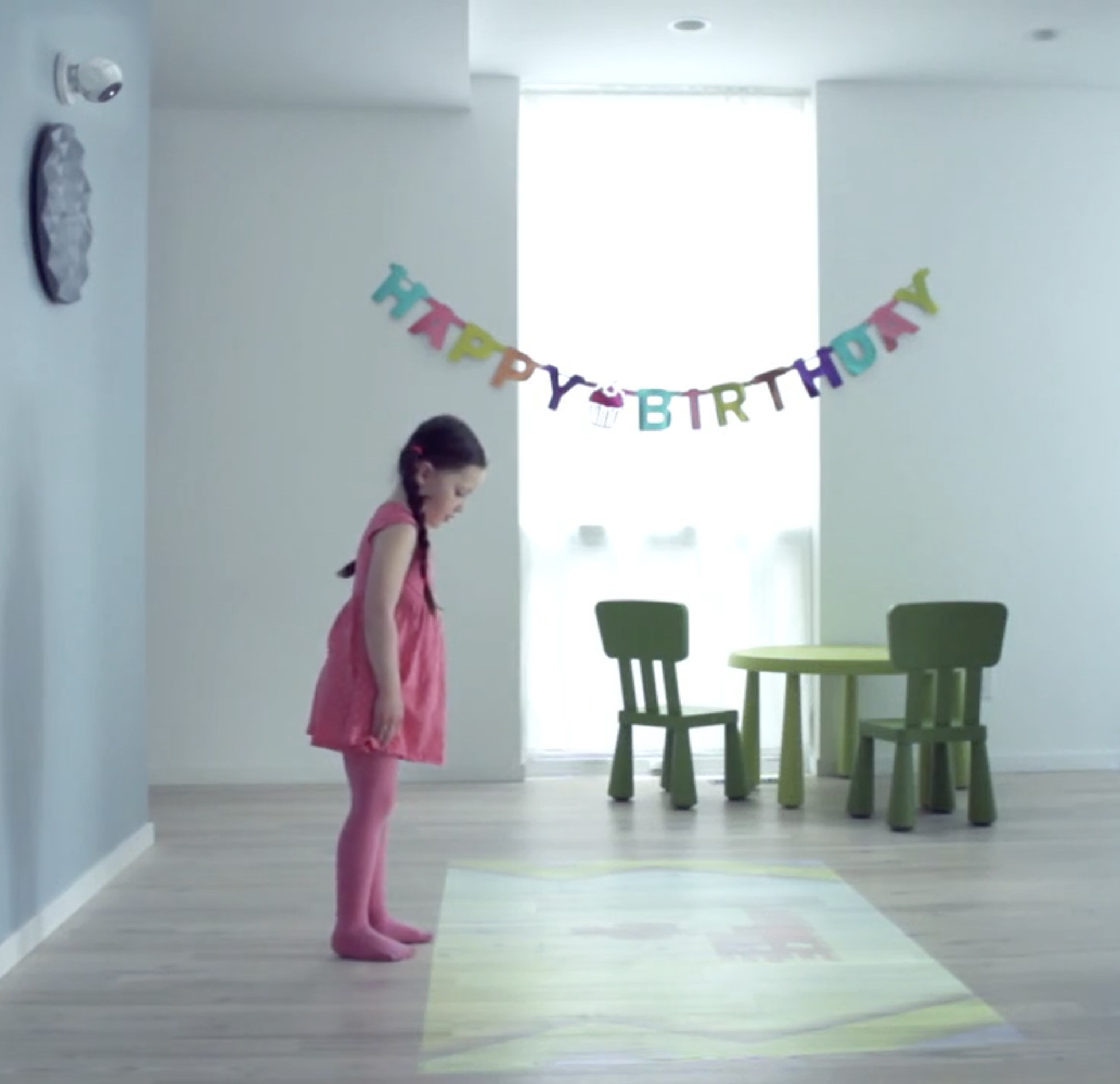 young girl looking at a floor projection with happy birthday on the wall behind her